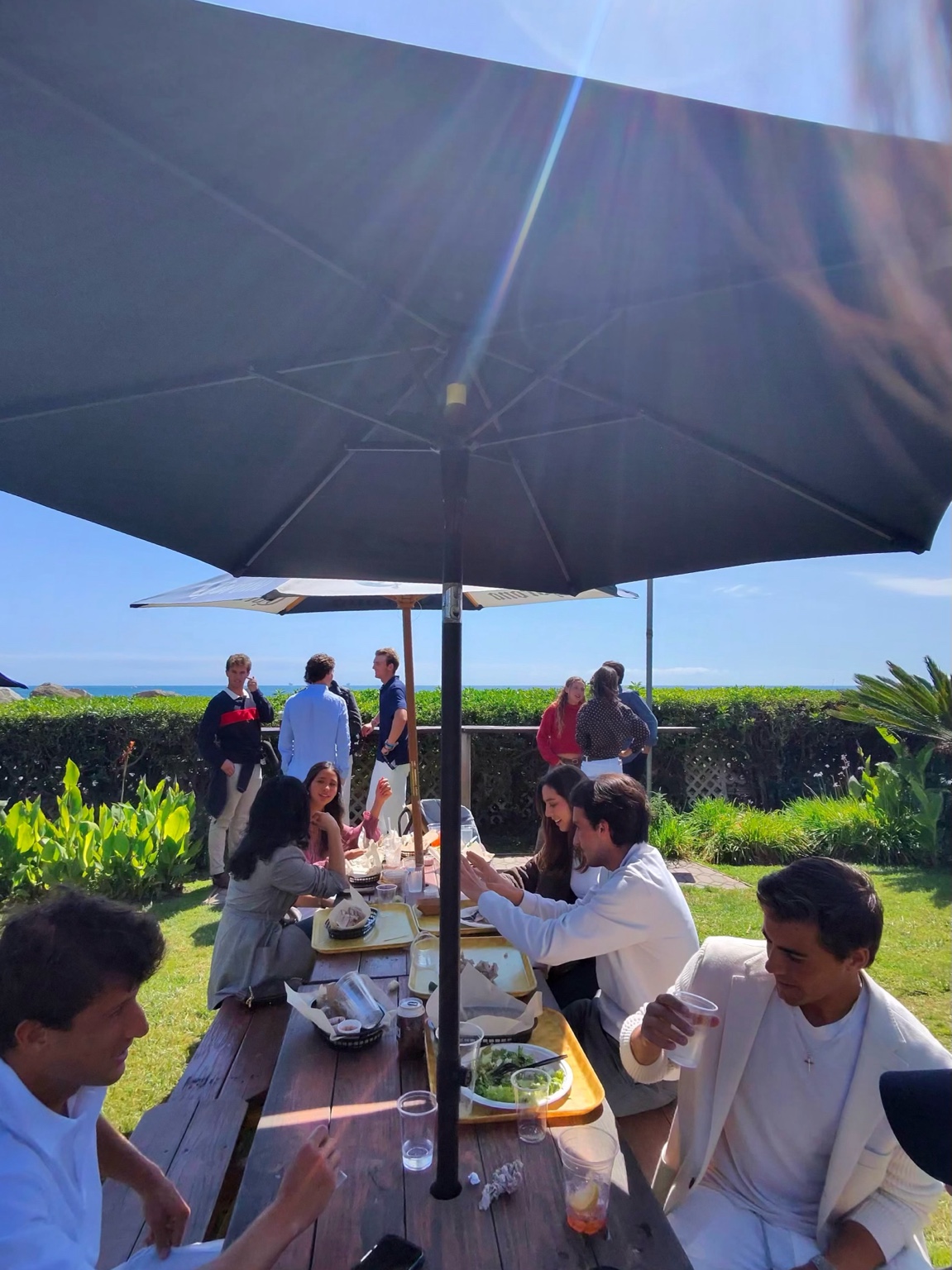 Community members sharing lunch under umbrellas by the ocean